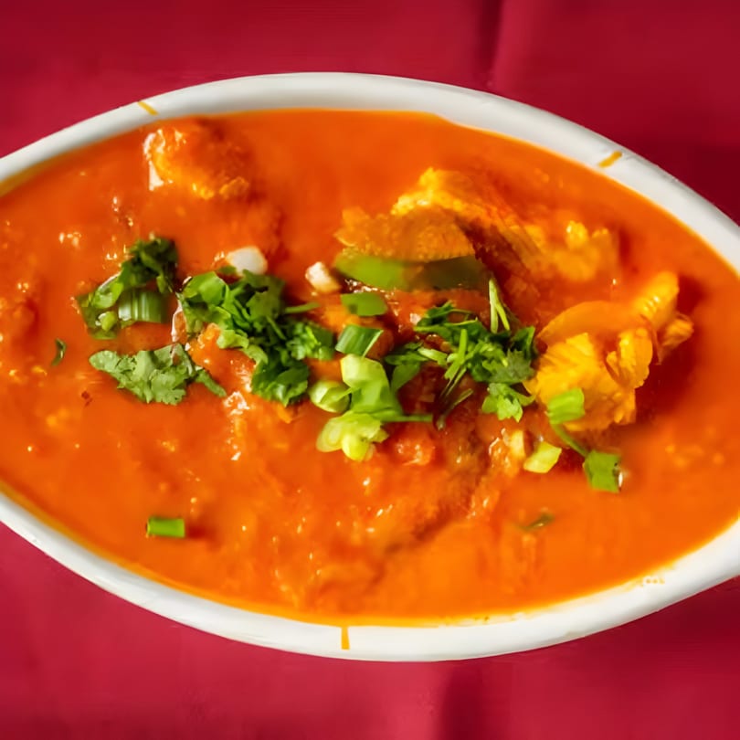 Mirch Masala's vibrant orange Indian curry, garnished with fresh green herbs, in a white oval bowl.