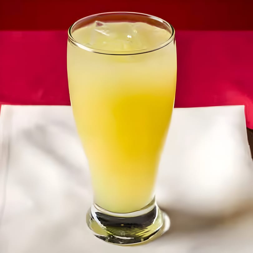 A tall glass of yellow lemonade with ice, set against a red and white background.